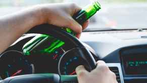 A close view of a driver's hands holding a green bottle of beer