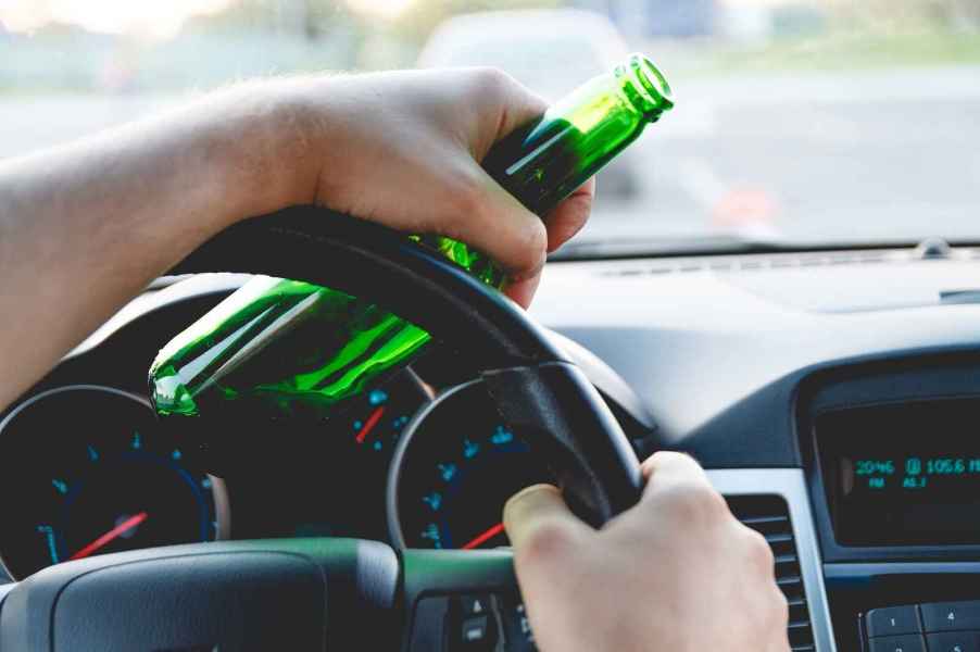 A close view of a driver's hands holding a green bottle of beer