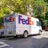 A FedEx delivery truck driving alone a busy residential New York street