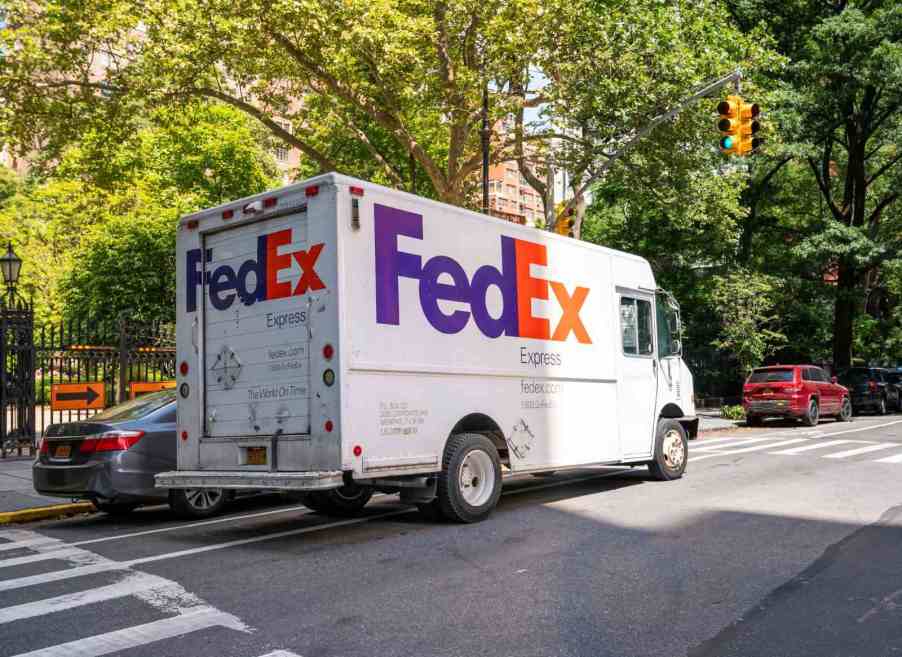 A FedEx delivery truck driving alone a busy residential New York street