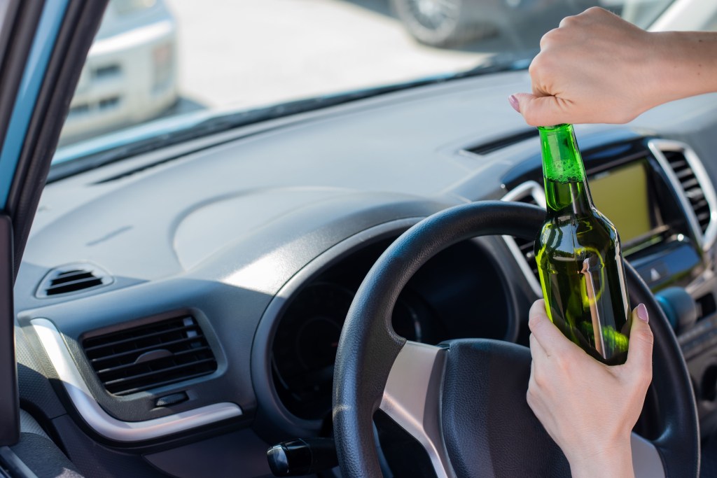 A woman opening a beer while driving