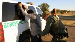 A Border patrol agent searching a man near an SUV