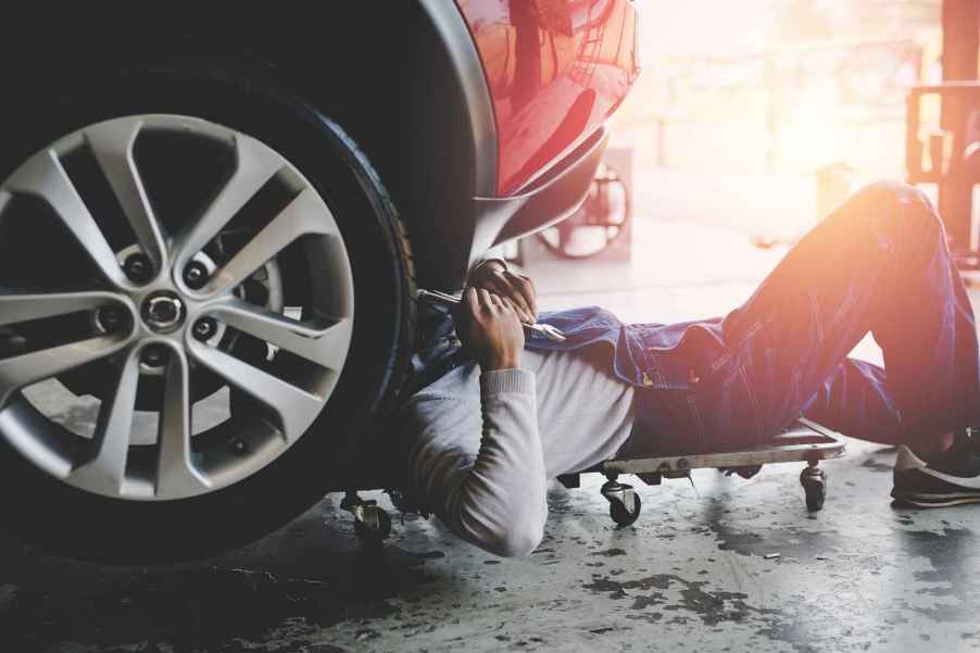 Mechanic in denim overalls lays under a car's front end