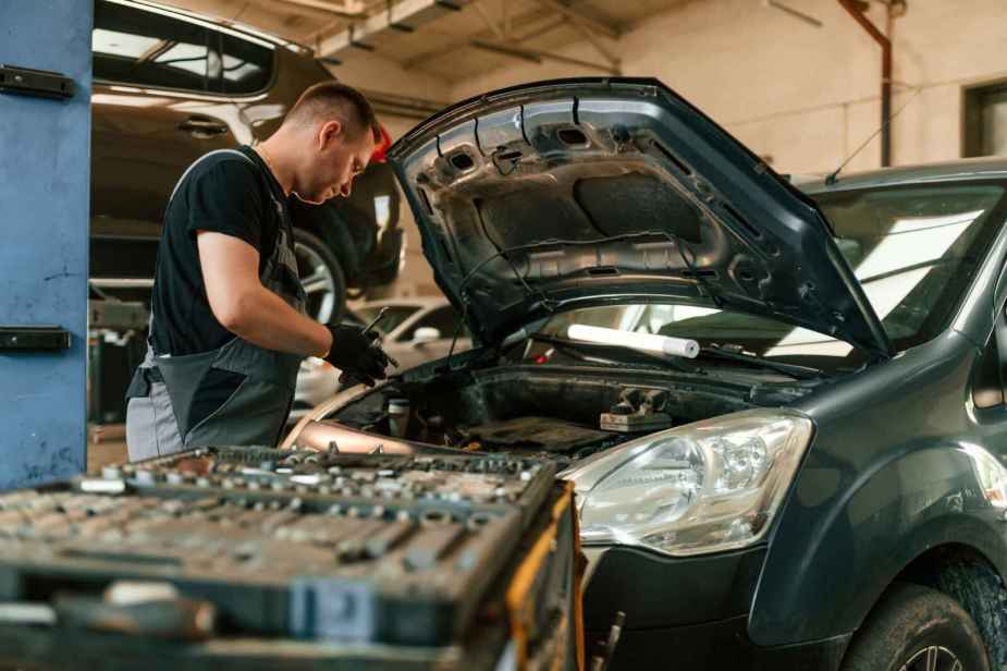 An automotive technician leaning over a vehicle using a wrench, with a cart full of tools at the ready