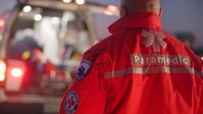 A paramedic in uniform standing in front of the back of an ambulance