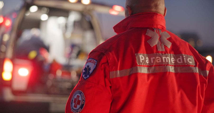 A paramedic in uniform standing in front of the back of an ambulance