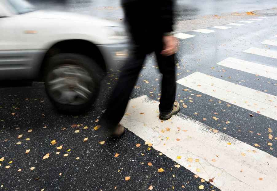 A man crossing the street in a crosswalk with a speeding car heading towards him, implying an imminent collision between the car and the pedestrian