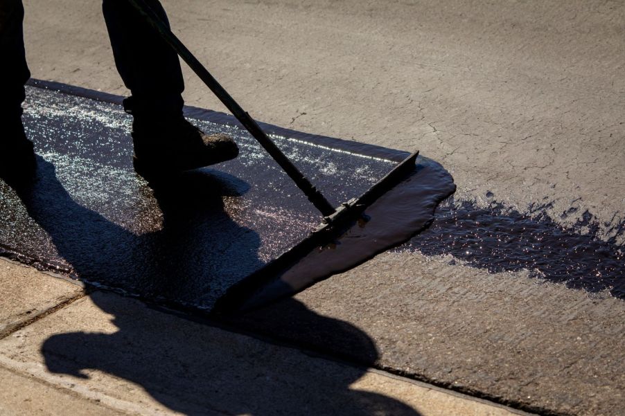 A man pushing a flatbrush to evenly distribute sealcoating on a road