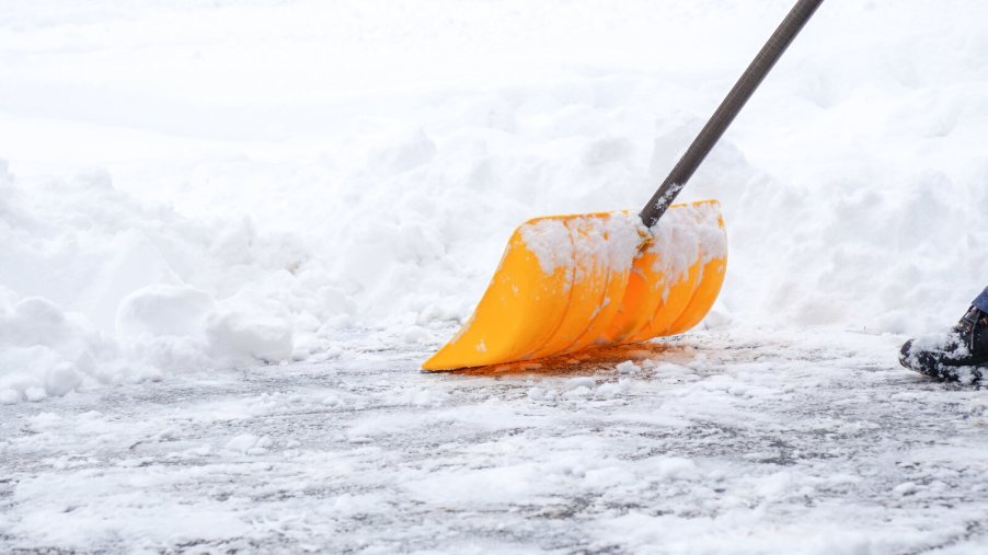 A person shoveling snow on a driveway in close view of the yellow shovel
