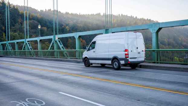 A white van traveling down a scenic driveway