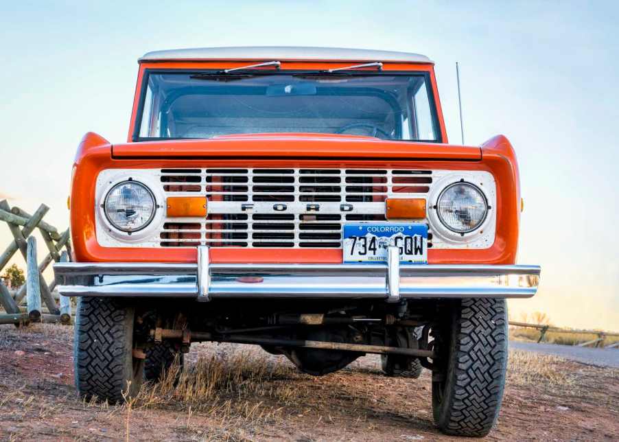 Orange 1972 Ford Bronco parked in a field, the sky visible in the background.