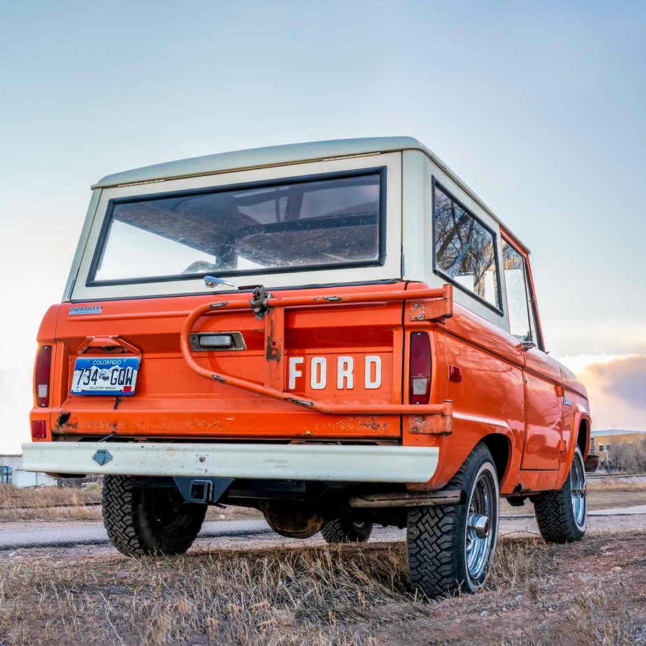 The back of an orange, first-gen Ford Bronco SUV parked by a mountain trail.