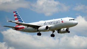 Gray American Airlines jet in front of a blue sky and clouds.