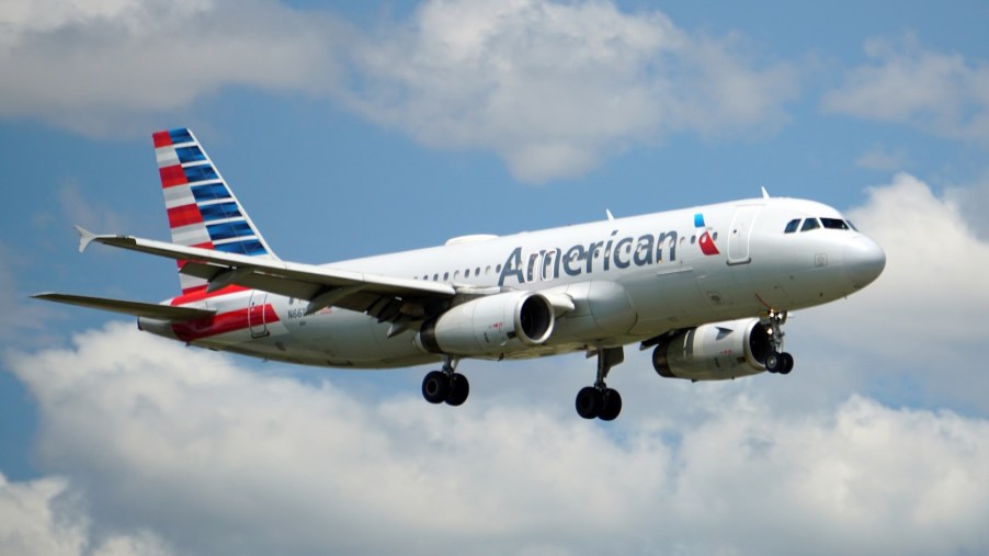 Gray American Airlines jet in front of a blue sky and clouds.