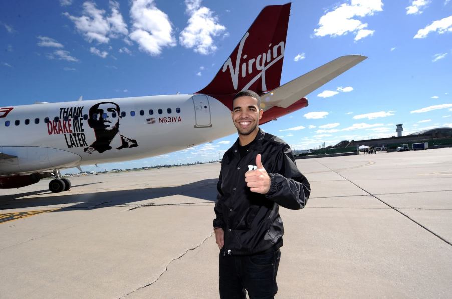Rapper drake stands on an airport runway, Virgin America plane visible in the background.