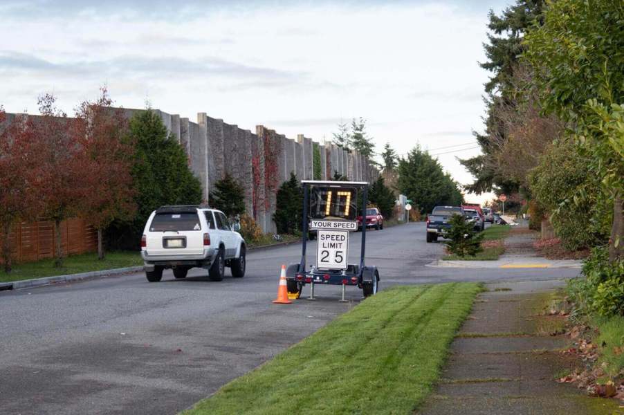An SUV drives past a speed limit sign with an electronic indicator.