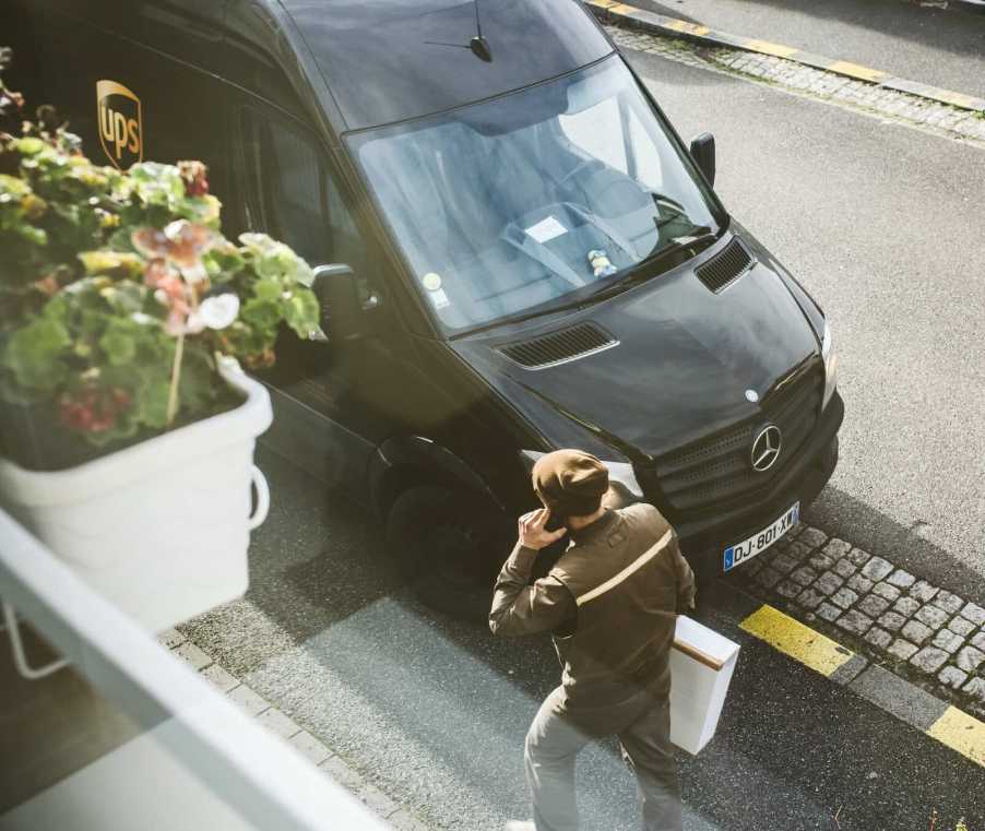 Overhead view of a UPS driver delivering a package, his truck visible in the background