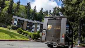 UPS delivery person driving away in a brown truck, an apartment building visible in the background.