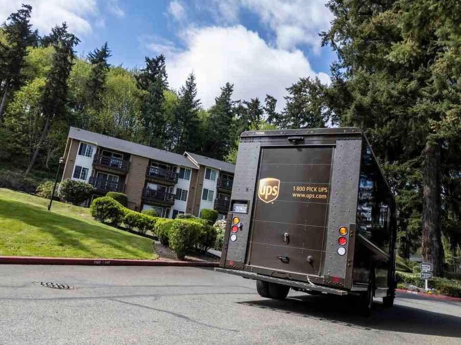 UPS delivery person driving away in a brown truck, an apartment building visible in the background.