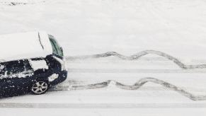 A black car driving on snowy, ice-covered road with slide marks behind it