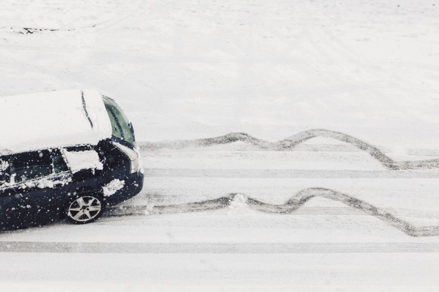 A black car driving on snowy, ice-covered road with slide marks behind it