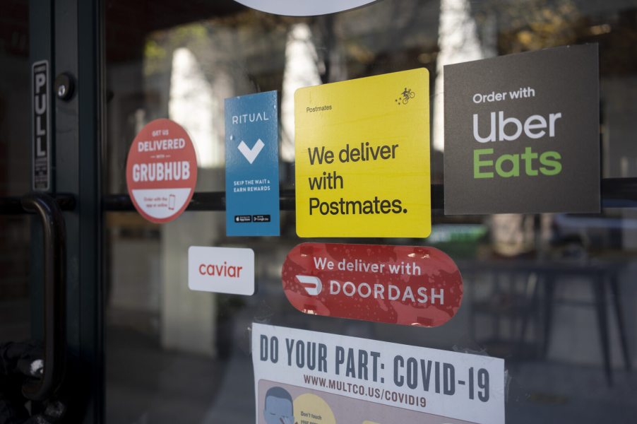 DoorDash sticker plus other food delivery services on a retail storefront glass door