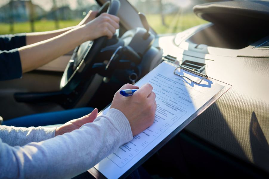 A drivers licensing exam taking place inside a car in close view of the driver and instructor arms