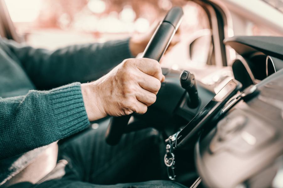 Elderly person's hands driving a car in close side view