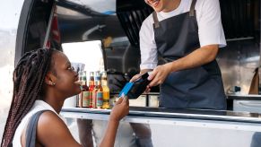A customer buying food from a food truck, and a worker taking her card to process a payment