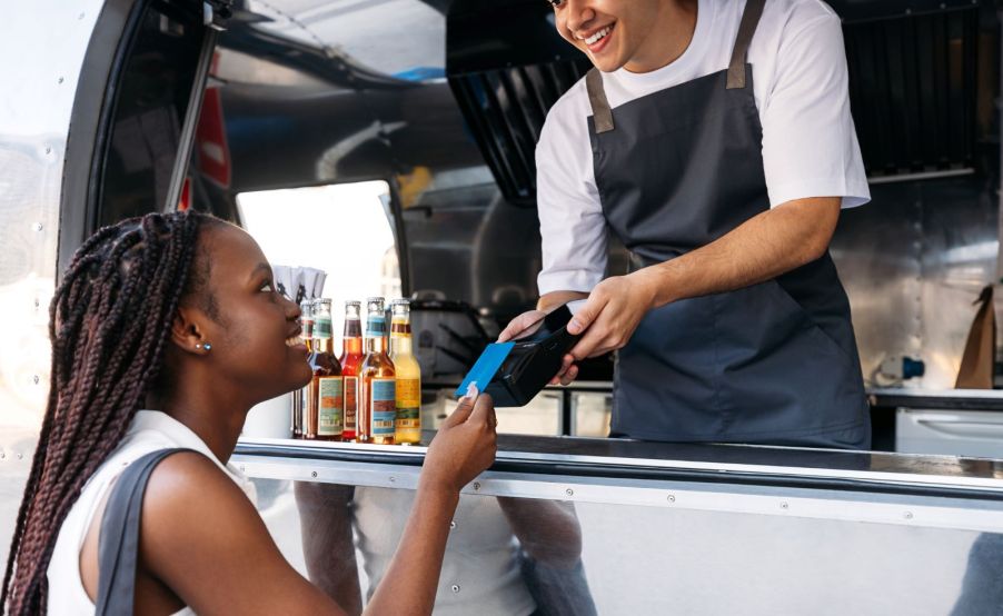 A customer buying food from a food truck, and a worker taking her card to process a payment