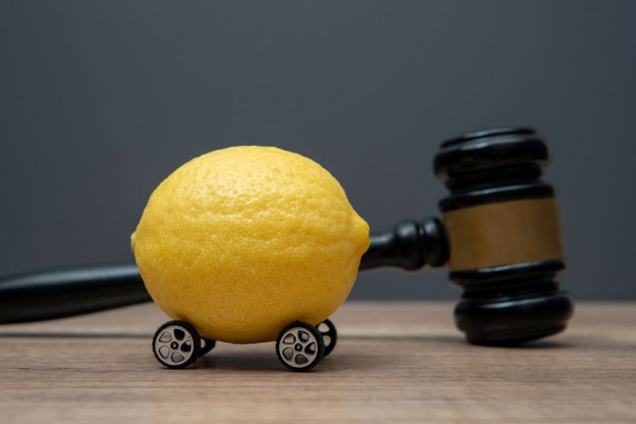 A lemon with four wheels underneath made to look like a car, with a judge's gavel in the background to symbolize "lemon law"
