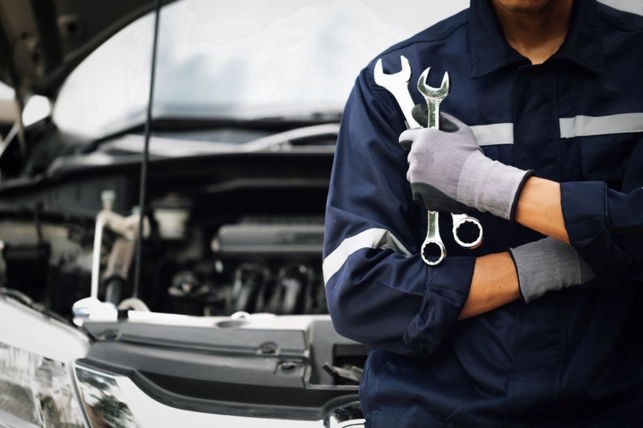 A mechanic standing in front of a car holding wrenches