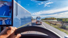 A semi truck driver behind the wheel, traveling with another truck hauling liquid