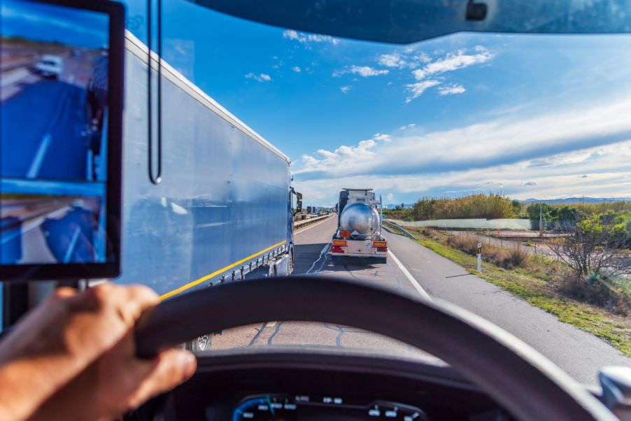 A semi truck driver behind the wheel, traveling with another truck hauling liquid
