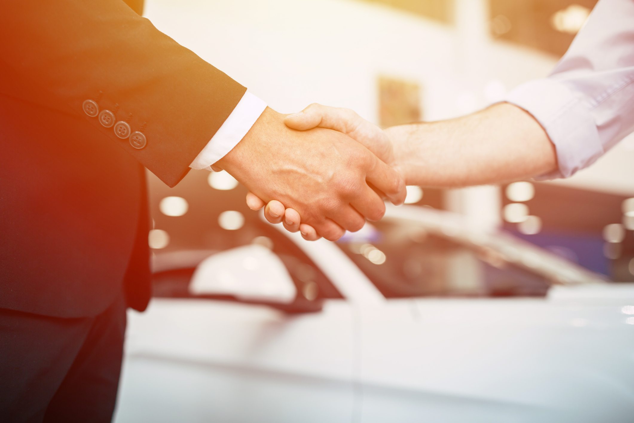 Two men shake hands over a used car sale view from elbows to waist