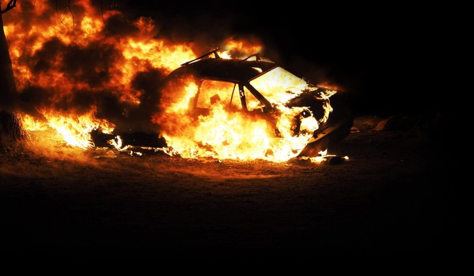 A car fire sends flames and smoke into the air.