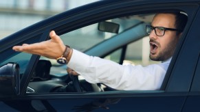 Man with glasses and white shirt gesturing while driving in road rage traffic.