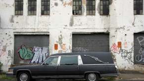 Black hearse car parked in front of a Brooklyn building covered in graffiti.