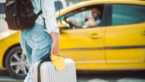 Woman with luggage flags down a driver of a yellow taxi cab.
