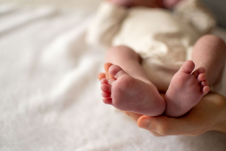 A newborn baby's feet, cradled by the mother's hands