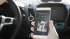 Hand holding a cell phone inside a car playing a music track connected to Bluetooth in close view