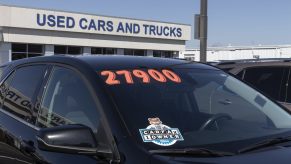 A used car dealership exterior sign reading "USED CARS AND TRUCKS" with a black car for sale in the foreground in close view