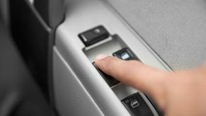 A man's finger resting on the window switch of a car