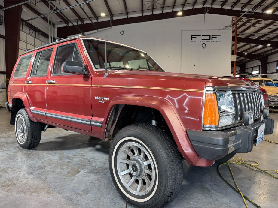 A rust-colored 1985 Jeep XJ Cherokee parked in low right front angle view in a garage