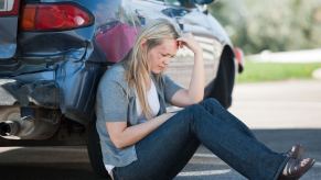 Sad driver sits by car totaled by insurance after minor fender bender accident.