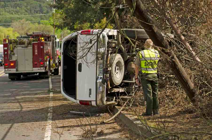 White Ford Super Duty pickup truck rolled over, fire fighter visible in the foreground.