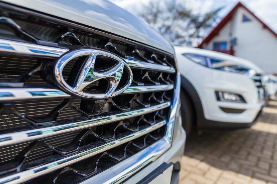 The chrome Hyundai logo on the badge of a crossover SUV in a dealership lot with a top IIHS safety award.