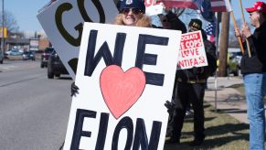Woman protester holding up a we heart Elon sign for a counter-protest outside a dealership.