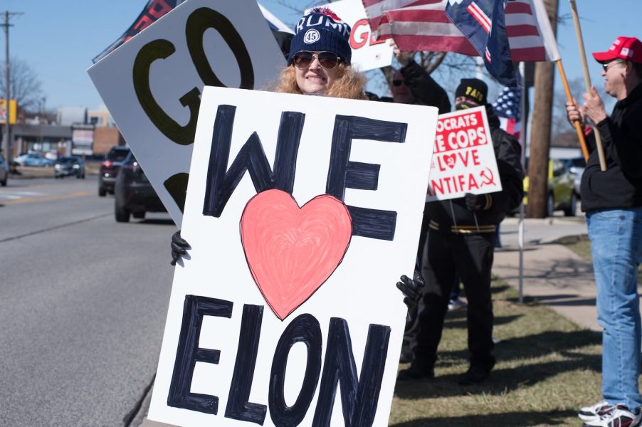 Woman protester holding up a we heart Elon sign for a counter-protest outside a dealership.