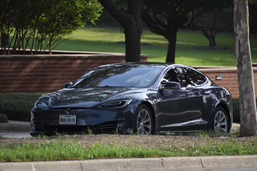 Black used Tesla car parked in a neighborhood, its value depreciation faster than Maserati